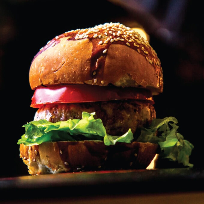 A close-up of a juicy double beef burger with melted cheese and fresh vegetables from Let's Fry Away.