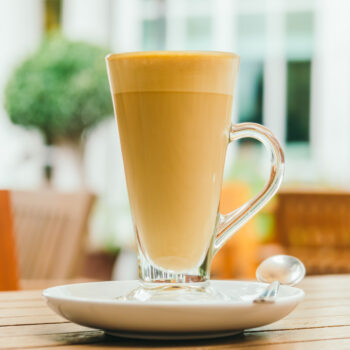 A steaming, rich brown ceramic mug of authentic, milky African Tea infused with visible ginger pieces and spices, resting on a woven coaster at a rustic table in Kilimani by Let's Fry Away.