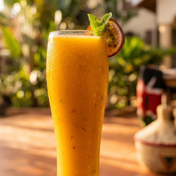 A tall, chilled glass of thick mango-passion fruit juice with condensation and a mint sprig, ready for delivery in Kilimani by Let's Fry Away."